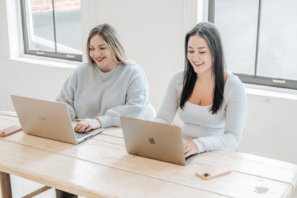 Chanel and Adrianna of Wellness Wave Marketing working on laptops at a table
